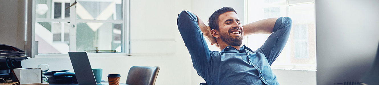 Man in office smiling and leaning back in computer chair. 